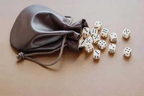 Set of gaming dice rolled out of leather bag on brown background. Concept wit Stock Photos