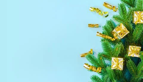 A set of gold gift boxes and a streamer lie on spruce branches on a blue Stock Photos