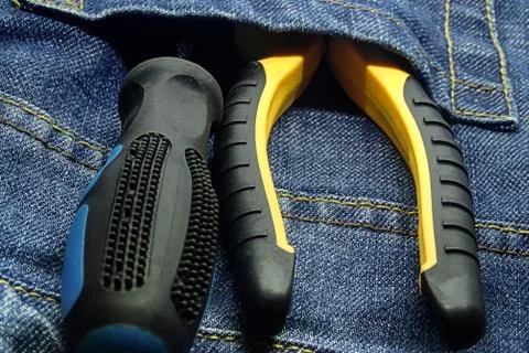 Set of hand tools screwdriver yellow black pliers pocket of jeans close-up Stock Photos