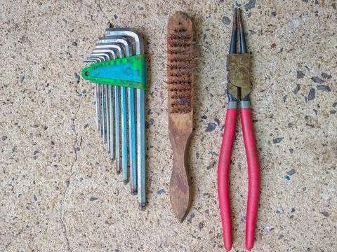 Set of hex keys, wire brush, and red pliers arranged neatly on concrete floor Stock Photos