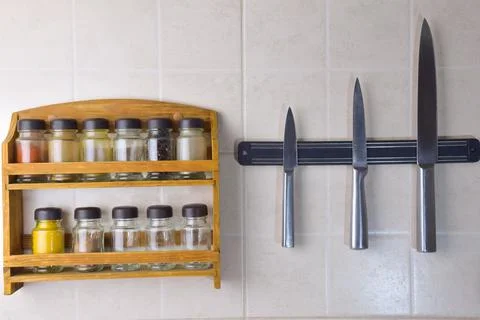 A set of jars with different spices and a set of three steel knives hang Stock Photos