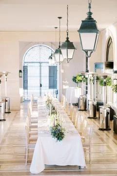 Set long festive table with candles and bouquets of flowers in the large hall of Stock Photos