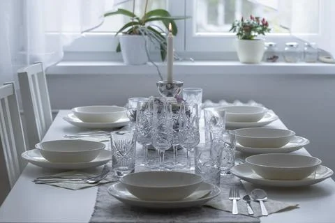 A set lunch table with glasses, plates, lighted candle and a window in the .. Stock Photos