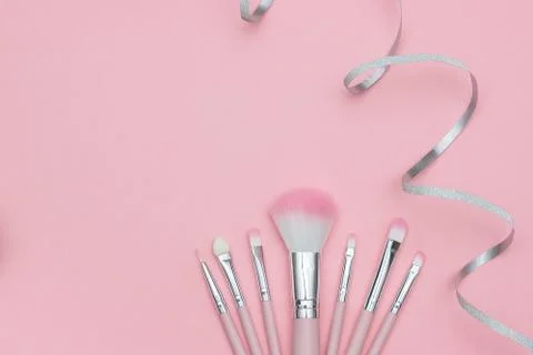 Set of makeup brushes and silver ribbon serpentine on pastel pink background Stock Photos