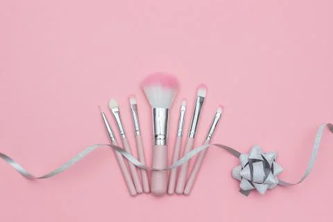 Set of makeup brushes and silver ribbon serpentine with bow on pastel pink ba Stock Photos
