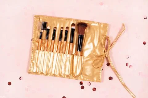 Set of makeup brushes in a gold case on festive pink background. Stock Photos