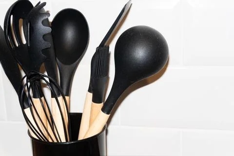 Set of modern black kitchen utensils with wooden handles on white ceramic tile Stock Photos