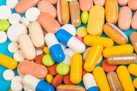 Set of multi-colored tablets and capsules on a blue background - Image Stock Photos
