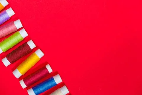 A set of multi-colored threads for sewing with an empty space for text on a red Stock Photos