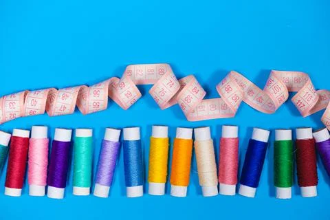 A set of multi-colored threads for sewing and a measuring tape on a blue Stock Photos