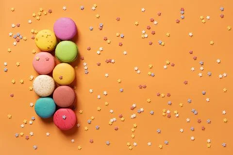 Set of multicolored macaroons on an orange background with small stars. Stock Photos