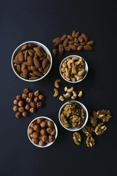 A set of nuts in white cups on a black background. Peanuts, hazelnuts and a.. Stock Photos