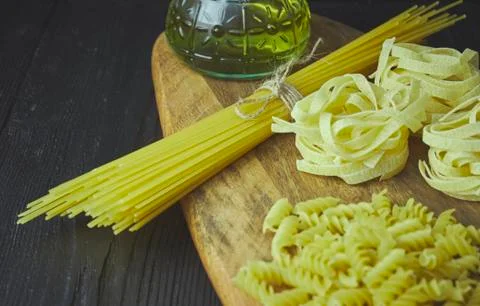 Set of raw pasta frame. Uncooked spaghetti, fusilli, fettuccine on a dark woo Stock Photos