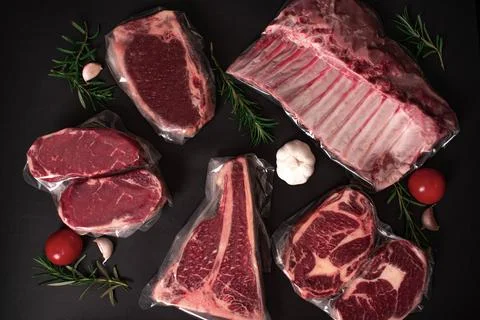 Set of raw vacuum-packed premium meat cuts on a black background. Stock Photos