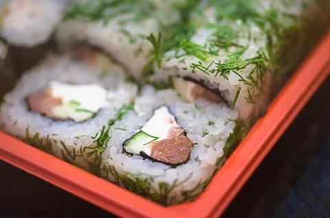 Set salmon rolls in a plastic plate on a black background Stock Photos