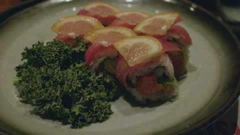 A set of salmon sushi rolls topped with lemon slice and served with salad leaves Vídeo Stock 286090147