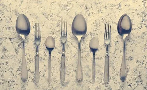 Set of silver spoons and forks on textured surface Stock Photos