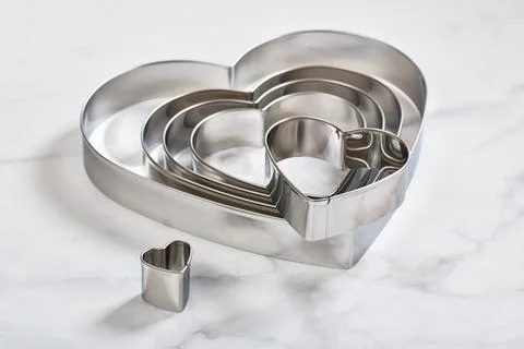 Set of stainless steel heart-shaped cookie cutters on a white marble surface Stock Photos