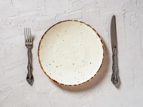 Set table. White speckled dinner plate between elegant table knife and fork. Stock Photos