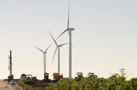 Set of three wind turbines and other heavy machinery used for the assembly of Stock Photos