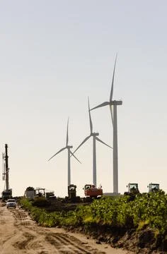Set of three wind turbines and other heavy machinery used for the assembly of Stock Photos