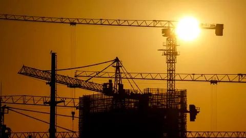 A set of tower cranes under construction in a city at sunset Stock Photos