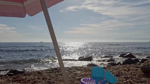 Set Of Toy Bucket With Rake And Shovel Under Parasol At The Beach. wide Stock Footage 255117419