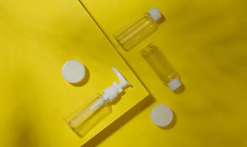 A set of transparent plastic bottles and jars with white lids on a yellow b.. Stock Photos