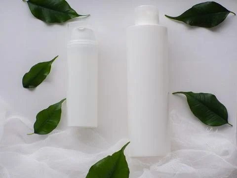 Set of two white bottles and green leaves on white background Stock Photos
