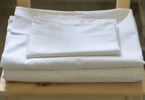 A set of white bed linen is lying on a chair. Stock Photos