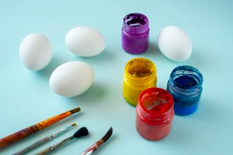 A set of white clean eggs, blue, yellow and red paints and brushes on bright  Stock Photos