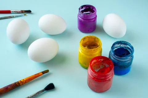 A set of white clean eggs, blue, yellow and red paints and brushes on bright  Stock Photos