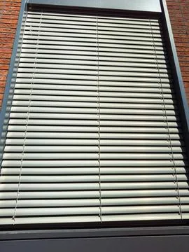 A set of window blinds blocks light from entering the building as sunlight hi Stock Photos