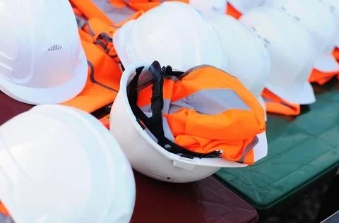 Sets of white construction helmets and orange vests at a construction site, no Foto stock