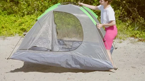 Setting up gray and green freestanding tent on sandy ground with green foli.. Vídeo Stock 331200059