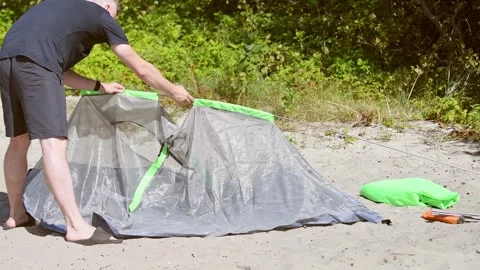 Setting up lightweight green and gray mesh tent on sandy ground near greenery Vídeo Stock 331200814