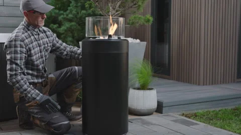 Setting up an Outdoor Fire Pit Heater for a Cozy Evening in a Backyard Garden Stock Footage 308534976