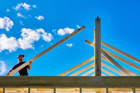 Setting rafter onto ridge beam and wall plate, young builder positions roof.. Stock Photos