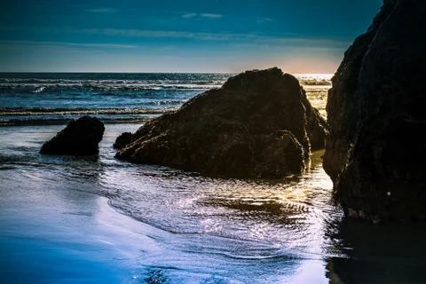 Setting sun backlight rock formations in shallow water at the beach Stock Photos
