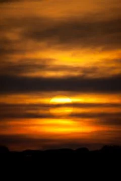A setting sun behind layers of cloud and deep orange sky tones   Stock Photos