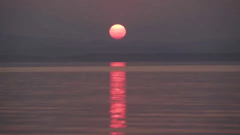 The setting sun behind the mountains reflected in the water Stock Footage 136330330