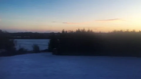 Setting Sun casts a bright orange glow over snow covered countryside landscape 動画素材 84676604