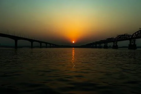 The setting sun, centered between the dark of two river bridges Foto stock