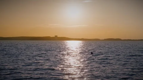 Setting sun creating warm colors in the sky over rippling water Stock Footage 292868858