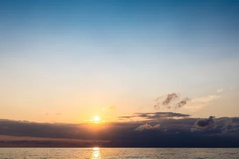 Setting sun in dark sky over low clouds and sea Stock Photos