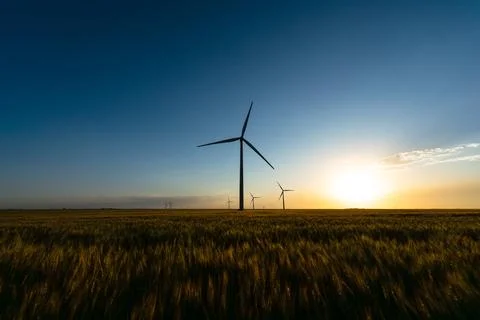 Setting sun glows over a wind farm and peaceful wheat fields, creating a dram Stock Photos