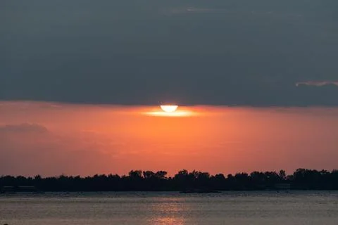 Setting sun half hidden by clouds over ocean Stock Photos