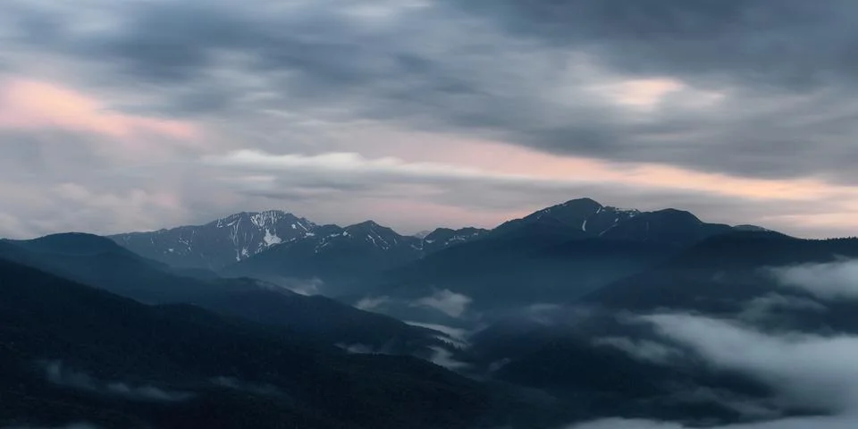 The setting sun illuminates the clouds over the mountain peaks of the caucasus Stock Photos