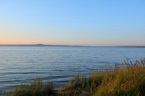 The setting sun illuminates the high hills surrounding a large lake with re.. Stock Photos