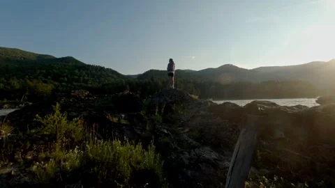 The setting sun illuminates the mountains and the turbulent river. The girl Stock Footage 278365811